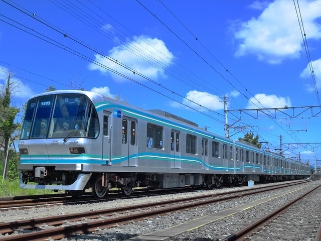 真夏の青空にウェーブデザインの識別帯が映える9000系リニューアル車。